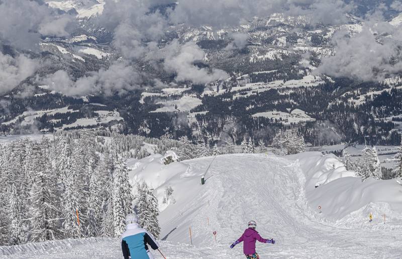 <p>Eine Frau auf Skiern und ein Kind am Snowboard fahren im Sonnenschein die perfekt präparierte und tiefverschneite Skipiste hinunter. Der Himmel ist blau nur über dem Tal sind ein paar Wolken zu sehen. Dieses Bild entstand im Skigebiet Nassfeld in Kärnten, dem Skigebiet an der Grenze zu Italien, welches auch zu den "TOP 10 Skigebieten" Österreichs gehört.</p>
